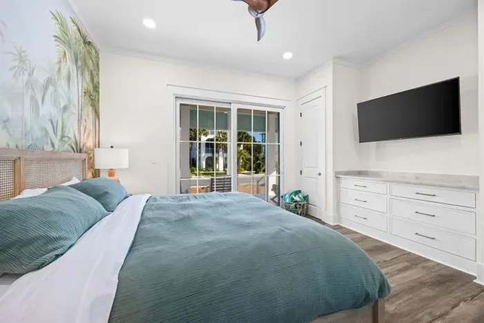 Primary bedroom with porch access (daytime view shown prior to drapery install), built-in dresser, and 55" TV