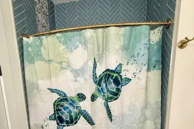 Spot the sea turtle on the shower curtain — a nod to island getaways in this guest house bath. The palm-and-toucan mural next door carries the same tropical spirit.