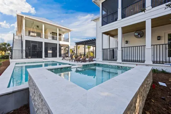 Step into the raised spa and watch it spill straight into the pool below — hot tub and pool working together, with both homes framing the scene behind you.