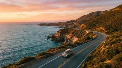 Vintage car drives scenic coastal highway at sunset