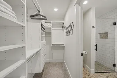 Spacious walk-in closet with built-ins beside a sleek tiled shower