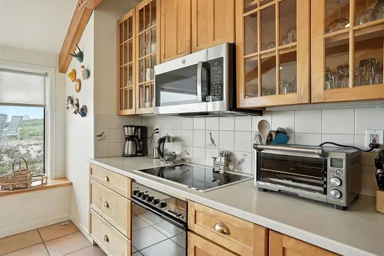 - Bright kitchen with wood cabinetry, large windows & modern appliances for easy cooking  - Features electric cooktop, microwave, toaster oven & coffee maker for convenience  - Scenic dune views create a relaxing atmosphere while you prepare meals
