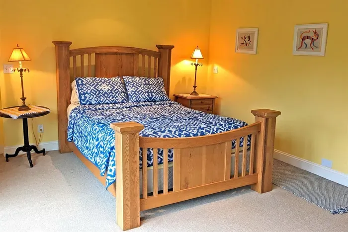 - Cozy bedroom with wooden bed frame, blue patterned bedding, and warm lighting  - Soft yellow walls add brightness and a cheerful touch to the space  - Includes nightstands with lamps for evening reading or ambiance