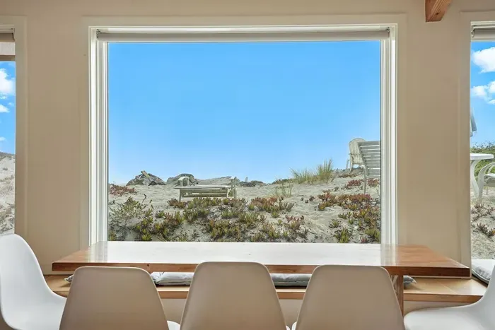 - Dining area with stylish picture window overlooking the sandy dunes  - Wooden table with white chairs provides the perfect setting for any meal  - Unobstructed views create a serene and picturesque dining experience
