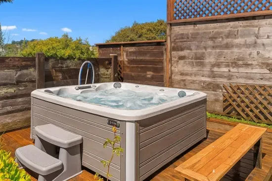- Private hot tub area with wooden deck and seating for relaxation  - Surrounded by fencing and greenery for added privacy and comfort  - Perfect spot to unwind after a day of beach walks or local adventures