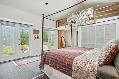 - Spacious bedroom with four poster bed, patterned bedding, and loft space above for extra charm  - Double glass doors open to a private patio with garden views  - Neutral tones and natural light create a warm, inviting retreat