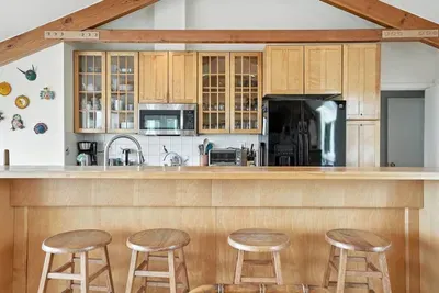 - Kitchen and breakfast bar combo with seating for four, perfect for casual dining  - Features wood paneled cabinetry, black refrigerator, and open shelving style  - Exposed beams and wall decor create a warm, welcoming coastal kitchen vibe