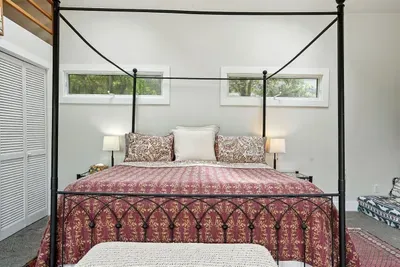 - Cozy sleeping area with elegant four poster bed and patterned quilt  - Side windows bring in natural light while providing privacy  - Simple decor and warm lighting make it a restful and comfortable space