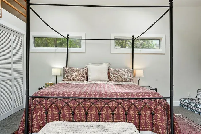 - Cozy sleeping area with elegant four poster bed and patterned quilt  - Side windows bring in natural light while providing privacy  - Simple decor and warm lighting make it a restful and comfortable space
