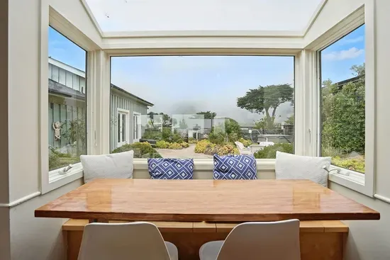 - Dining nook with panoramic windows overlooking the garden courtyard  - Wooden table paired with modern chairs and cozy bench cushions  - Inviting spot for meals while enjoying views of the outdoors year round