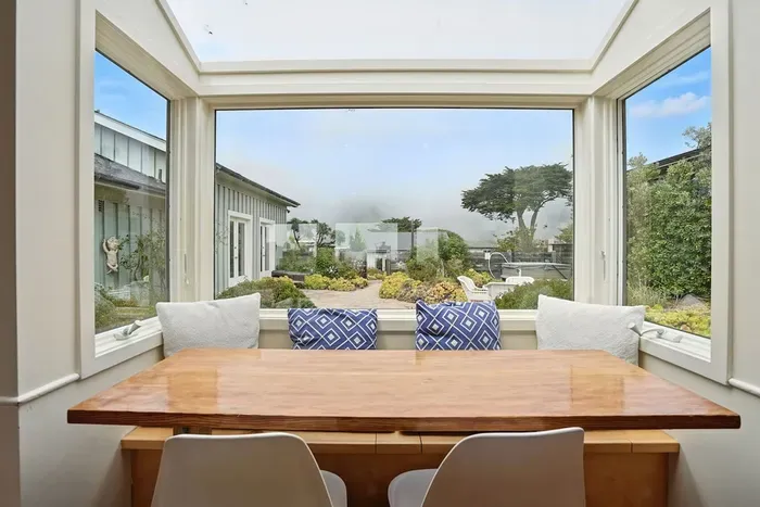 - Dining nook with panoramic windows overlooking the garden courtyard  - Wooden table paired with modern chairs and cozy bench cushions  - Inviting spot for meals while enjoying views of the outdoors year round