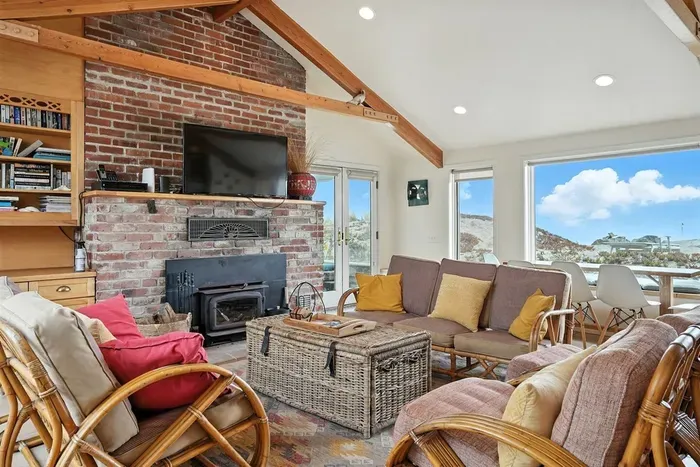- Inviting living area with brick fireplace, flat screen TV, and rattan seating  - Vaulted ceilings and exposed beams add rustic coastal charm to the space  - Perfect for gathering after a day of beachside adventures