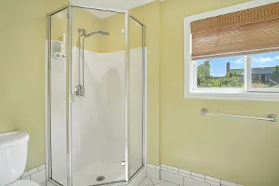 - Bright bathroom with corner glass shower and sleek fixtures for a modern touch  - Window with bamboo shade allows soft daylight while maintaining privacy  - Light yellow walls create a cheerful and inviting atmosphere