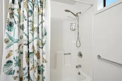 - Fresh white bathroom with tub and shower combination for versatile use  - Coastal pattern shower curtain adds a fun, decorative touch  - Includes window for natural light and a clean, bright feel