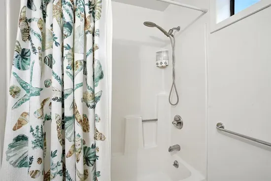 - Fresh white bathroom with tub and shower combination for versatile use  - Coastal pattern shower curtain adds a fun, decorative touch  - Includes window for natural light and a clean, bright feel