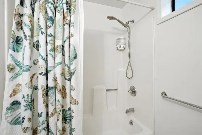 - Fresh white bathroom with tub and shower combination for versatile use  - Coastal pattern shower curtain adds a fun, decorative touch  - Includes window for natural light and a clean, bright feel