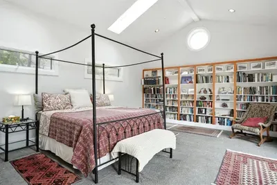 - Airy bedroom with four poster king bed, patterned bedding, and cozy bench at foot  - Wall to wall bookshelves stocked with reading selections for a relaxing stay  - Skylights and round window fill the space with soft natural daylight