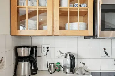 - Coffee station with drip coffee maker, electric kettle, & essential supplies for your morning  - Glass front cabinets neatly display cups, plates, & bowls for easy access  - Decorative tile accents with coastal bird designs add charm to the space