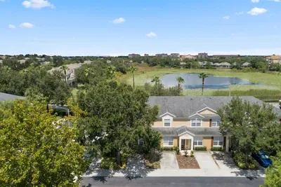 Aerial view of townhouse with nearby pond and trees.