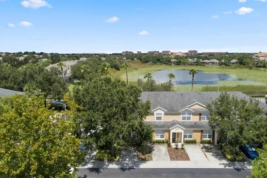 Aerial view of townhouse with nearby pond and trees.