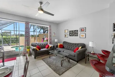 - Bright living room with plush gray sofas, vibrant red cushions, and wall art  
- Sliding doors open to the pool area for easy indoor outdoor flow and relaxation  
- Ceiling fan and natural light create a fresh, welcoming atmosphere year round