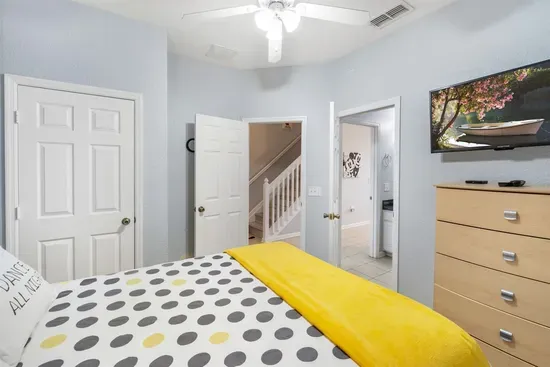 - Bright bedroom with modern polka dot bedding and cheerful yellow throw  
- Wall mounted TV and dresser provide convenience and entertainment  
- Access to hallway and stairway for easy movement throughout the home