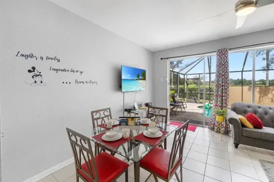 - Dining area with glass top table set for four beside sliding doors to the pool  
- Wall art and patterned curtains add playful style to the bright interior  
- Enjoy meals indoors with views of the screened in patio and sparkling pool