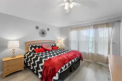 - Spacious bedroom with king bed, bold chevron bedding, and red accent throws  
- Large windows with sheer curtains let in soft natural light for a calm feel  
- Stylish wall art and nightstands with lamps enhance the cozy retreat