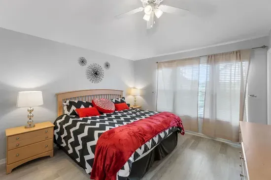 - Spacious bedroom with king bed, bold chevron bedding, and red accent throws  
- Large windows with sheer curtains let in soft natural light for a calm feel  
- Stylish wall art and nightstands with lamps enhance the cozy retreat