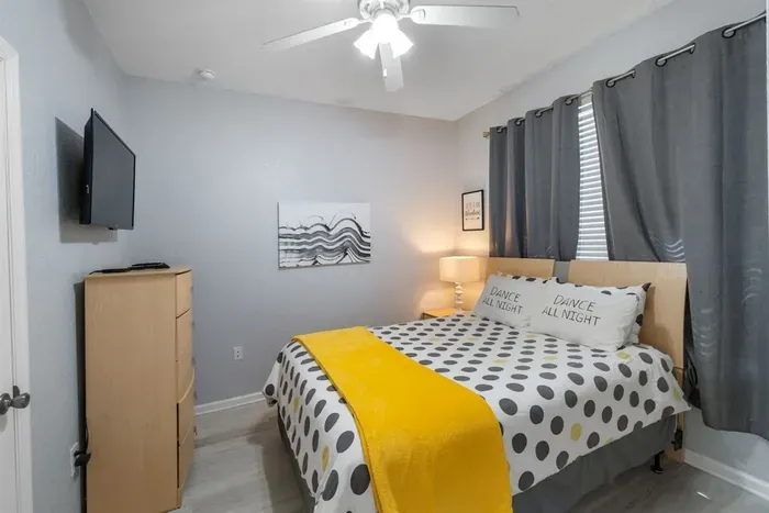 - Cozy bedroom with queen bed, modern polka dot bedding, and yellow throw  
- Soft lighting and ceiling fan create a comfortable and restful environment  
- Perfect for couples or solo travelers seeking a relaxing night’s sleep