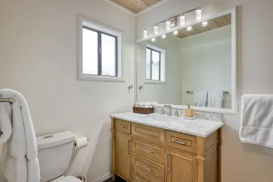 - Bathroom includes single sink vanity with wood cabinetry for storage  
- Wide mirror and bright lights make getting ready a comfortable routine  
- Window offers both natural light and ventilation throughout the day