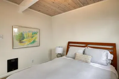 - Cozy bedroom with queen bed and crisp white linens for restful nights  
- Wooden headboard and bedside lamp offer a touch of classic style  
- Minimalist decor with bright artwork creates a calming atmosphere