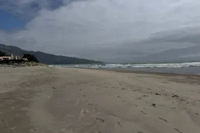 Wide sandy beach with waves and mountain views.