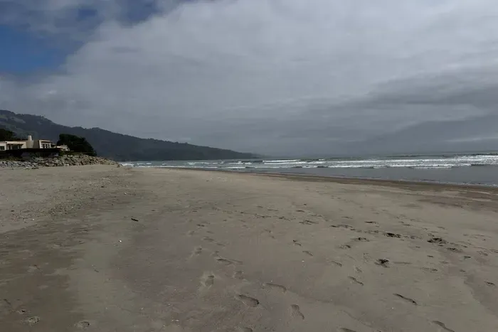 Wide sandy beach with waves and mountain views.