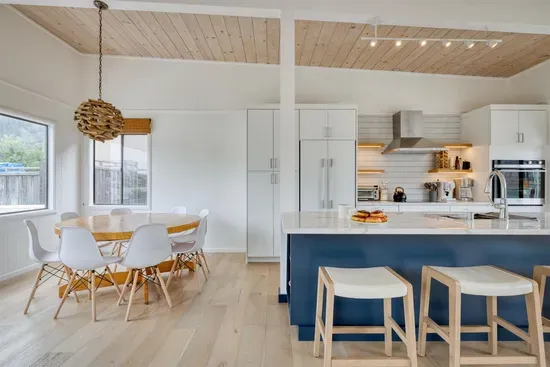 - Dining space with round table and modern chairs for shared meals  
- Kitchen features a navy island with bar seating for casual dining  
- Light wood flooring and ceiling create a warm, coastal inspired vibe