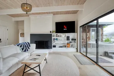 - Comfortable living area with fireplace, TV, and built in shelving decor  
- Sliding glass doors open directly to the patio and hot tub area outside  
- Soft neutral tones create a calming, welcoming atmosphere for guests