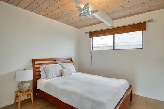 - Cozy bedroom featuring wooden bed frame with crisp white linens for rest  
- Wood paneled ceiling adds warmth and character to the inviting setting  
- Large window fills the space with daylight and neighborhood scenery