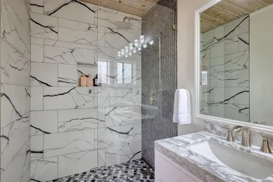 - Spacious bathroom with walk in shower featuring large marble style tiles  
- Bold black accents and mosaic tile floor add a modern, upscale touch  
- Glass enclosure keeps the space bright while showcasing elegant finishes