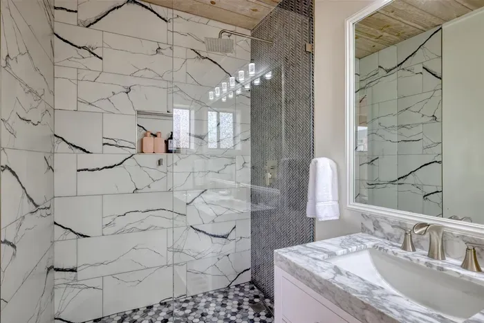 - Spacious bathroom with walk in shower featuring large marble style tiles  
- Bold black accents and mosaic tile floor add a modern, upscale touch  
- Glass enclosure keeps the space bright while showcasing elegant finishes
