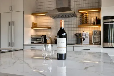 - Elegant kitchen island with marble countertop sets a refined tone  
- Bottle of wine and glass ready to welcome guests upon arrival  
- Modern backsplash, open shelving, and under cabinet lighting add flair