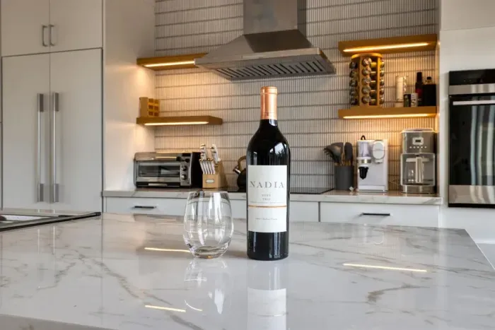 - Elegant kitchen island with marble countertop sets a refined tone  
- Bottle of wine and glass ready to welcome guests upon arrival  
- Modern backsplash, open shelving, and under cabinet lighting add flair