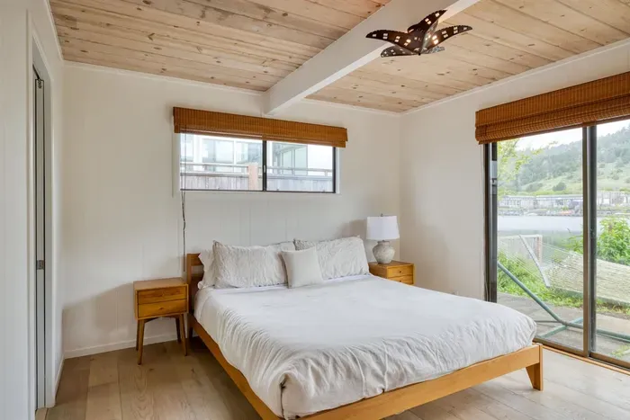 - Bright bedroom with queen bed and sliding glass doors to a waterfront patio  
- Wooden ceiling and matching furniture create a warm and inviting retreat  
- Large windows fill the room with natural light and scenic outdoor views