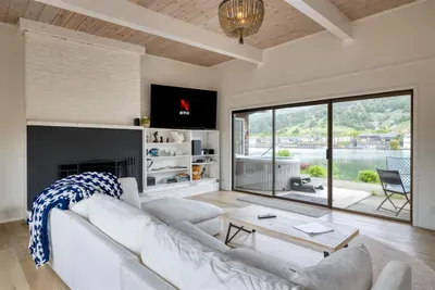 - Cozy living room with white sectional and sliding doors to the waterfront  
- Wall mounted TV with streaming access for entertainment anytime  
- Large windows flood the space with natural light and scenic views