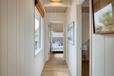 - Hallway with natural light from side windows leading to cozy bunk room  
- White paneled walls and wood ceiling create a fresh coastal inspired feel  
- Artwork adds character to this inviting passageway between bedrooms