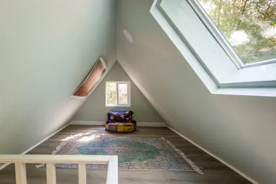 - Cozy loft nook with vaulted ceiling and large skylight for natural light
- Soft area rug creates a welcoming spot for reading or quiet retreat
- Unique triangular architecture adds charm and character to the space