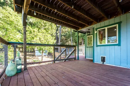 - Covered deck with warm toned wood flooring and open railing design  
- Overhead beams create a rustic charm perfect for relaxing afternoons  
- Peaceful setting with views of greenery and open space beyond the yard