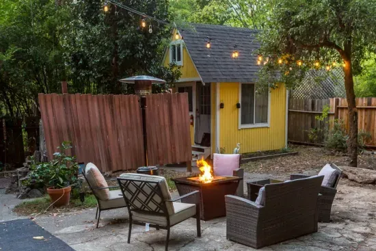 - Inviting outdoor lounge with fire pit surrounded by cushioned seating  
- String lights overhead create a magical glow for evening relaxation  
- Yellow garden shed adds cheerful charm to this private backyard escape