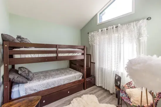 - Bright bedroom featuring sturdy wooden bunk beds with soft patterned bedding  
- High window paired with sheer curtains allows natural light to filter inside  
- Cozy corner space ideal for kids or extra guests seeking a comfortable stay