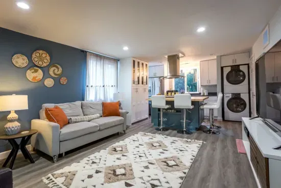 - Stylish open living area with blue accent wall and cozy gray sofa seating  
- Modern kitchen with breakfast bar seating for four and full appliances  
- Includes in unit washer and dryer for guest convenience during stays