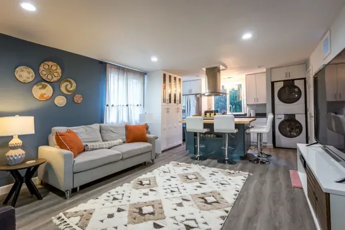 - Stylish open living area with blue accent wall and cozy gray sofa seating  
- Modern kitchen with breakfast bar seating for four and full appliances  
- Includes in unit washer and dryer for guest convenience during stays